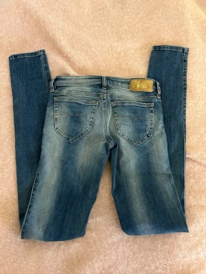 Blå skinny jeans från Diesel - Snygga blå skinny jeans från Diesel med klassisk femficksdesign och slitna detaljer. Jeansen har en ljus tvätt med subtila slitningar och Diesel-logga på bakfickan. Perfekta för dig som gillar en smal passform och vill ha ett par stilrena jeans i garderoben. Har fortfarande prislappen kvar. Nypris 1199.