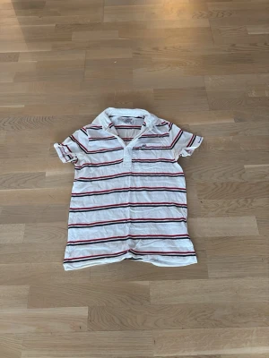 Vintage ralph rauren polo - Vit kortärmad pikétröja från Polo Jeans Co. Ralph Lauren med röda och svarta horisontella ränder. Skjortan har klassisk krage och knappar vid halsen. Tillverkad i mjuk bomull, perfekt för en avslappnad stil.