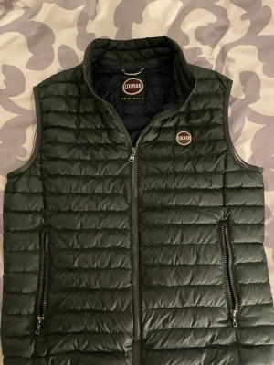 Mörkgrön dunväst från Colmar - Stilren mörkgrön dunväst från Colmar med quiltad design och hög krage. Västen har två dragkedjeförsedda fickor framtill och Colmar-logga på bröstet. Finns inga defekter. Kom med frågor o prisförslag