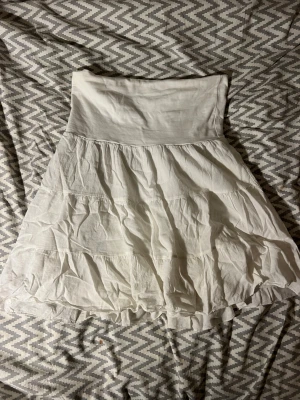 Vit volangkjol  - Säljer en söt vit kjol med volanger och bred linning. Kjolen är kort och har en luftig, flowy passform som är perfekt till sommaren☺️Köpt på smögen, västkusten från märket new collection. Står ingen storlek men skulle uppskatta S/M. Säljer en del andra somriga kläder så kika gärna in och skriv vid frågor!🥰