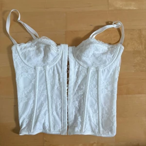 Vit spetskorsett med snörning - Säljer en vit korsett med vacker spets och justerbara axelband. Framsidan har hakknäppning och baksidan har snygg snörning för perfekt passform. Korsetten har bygel och dekorativa spetsdetaljer upptill 🌸🌸