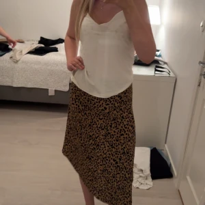 Leopardmönstrad omlottkjol med knyt - Säljer en snygg leopardmönstrad långkjol med omlottmodell och knyt i midjan. Kjolen har en beige bas med svarta leopardfläckar och är i ett lätt, flowy material som ger en cool vibe. Perfekt för dig som vill sticka ut med ett trendigt djurmönster.