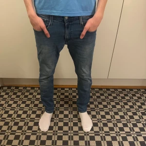 Replay jeans - Säljer ett par blå slim fit jeans med klassisk femficksdesign och snygga sömdetaljer på bakfickorna. Jeansen har en smal passform och är tillverkade i stretchigt denim för extra komfort. Perfekta för dig som gillar en modern och stilren look.