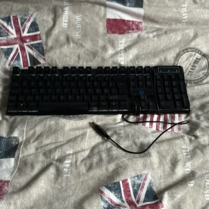  Gaming Keyboard - Nedis GCK51110BKND är ett USB-anslutet gamingtangentbord från 5-i-1 Gaming combo kit. Fullstort med numerisk del, tydliga tangenter och justerbara fötter. Tangentbordet är i gott skick med mindre tecken på användning. Perfekt för gaming och kontor.