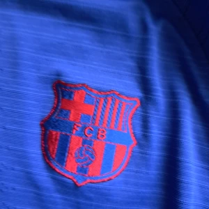 Blå FC Barcelona Nike fotbollströja M - Säljer en blå FC Barcelona fotbollströja från Nike i storlek M. Tröjan har korta ärmar, broderat klubbmärke på bröstet och Nike-logga i rött. Materialet är lätt och ventilerande, perfekt för träning eller match. Snygga detaljer med röd och vit text framtill.