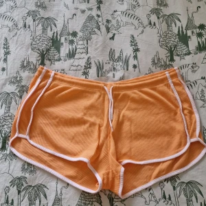 Orange shorts från Primark  - Snygga orange shorts från Primark i storlek XL. De har vit kant runtom och är gjorda i ett ribbat, mjukt bomullstyg. Perfekta för varma sommardagar eller när du vill chilla hemma. Sportig retrostil med rundade ben och elastisk midja. Oanvända och tvättade 1 gång.