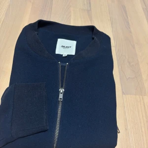Mörkblå bomberjacka från Object - Snygg mörkblå bomberjacka från Object med klassisk ribbad krage, muddar och dragkedja framtill. Jackan är i ett mjukt material och har en stilren look som passar perfekt till streetwear eller casual outfits. Hör av dig vid frågor 😊