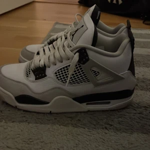 Nike Air Jordan 4 vit/svart US7 - Säljer ett par Nike Air Jordan 4 i vit och svart. Klassisk siluett med meshpaneler, snörning och Jumpman-logga på hälen. Skorna har en chunky sula och detaljer i svart och grått. Perfekta för dig som gillar streetwear och sneakers med ikonisk design. Dem har varit lite använda men är i gott skick ser nästan nya ut 