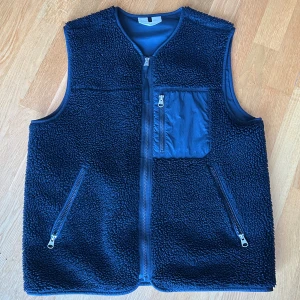 Arket fleeceväst  - Säljer en svart fleeceväst från Arket i storlek M. Västen har två snedställda fickor med dragkedja och en bröstficka i nylon. Perfekt för lager-på-lager och har en clean, sportig look med hel dragkedja framtill.