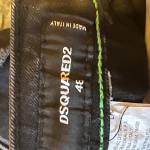 Svarta Dsquared2 jeans med slitningar - Svarta jeans från Dsquared2 med coola slitningar och färgstänk på framsidan. Klassisk femficksmodell med smal passform och snygga detaljer. Tillverkade i Italien och har en modern streetkänsla. Perfekta för dig som gillar en edgy look.