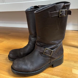 Johnny bulls skinnboots strl 38 mörkbruna - Johnny bulls skinnboots strl 38 mörkbruna. Har ej smörjt in skinnet sedan sist jag använde dem så de går säkert att putsa upp en aning om man vill. En del slitage med märken och veck finns (se bilder) Jag har strl 39, fotlängd 25cm och mig passar dem på. Nypris 1300kr.
