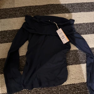 Mörkblå offshoulder topp - Säljer en mörkblå offshoulder topp från Gina tricot med långa ärmar. Toppen har en snygg, bred krage som vilar över axlarna och är tillverkad i mjuk bomull. Perfekt för dig som gillar stilrena och trendiga plagg.