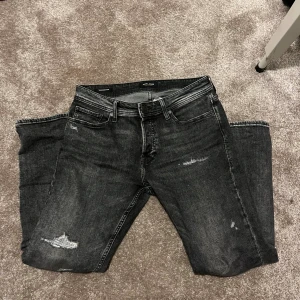 Grå jeans med slitningar - Säljer ett par grå jeans från Jack & Jones med snygga slitningar och en skön Straightfit passform. Jeansen är i storlek 30/30 och iprincip i nyskick! Nypriset är ungefär 800kr. Hör av er om ni har några frågor 