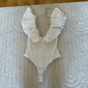 Vit body Zara  - Jätte snygg body från Zara med volanger! Sitter jätte snyggt på kroppen och så fin till fester! Köpte för runt 400kr. Använd typ två gånger men säljer för 230