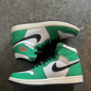 Nike Air Jordan 1 Retro gröna - Säljer ett par Nike Air Jordan 1 Retro High med grön och vit ovandel i skinn, svarta detaljer och klassisk svart swoosh. Skorna har svart snörning och en vit mellansula med svart yttersula. Perfekta för dig som vill sticka ut med en ikonisk sneaker.