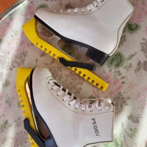 Peggy vita skridskor med gul skydd - Säljer ett par klassiska vita Peggy skridskor med högt skaft och snörning. Skridskorna har robusta stålblad och kommer med gula skydd. Yttermaterialet är skinn och insidan är vadderad för extra komfort. Perfekt för dig som vill glida fram på isen med stil.