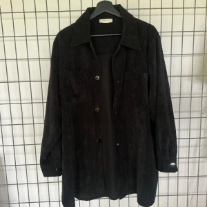 Stank Stockholm- Jacka/överskjorta, ribbad manchester - Stank Stockholm- Jacka/överskjorta i svart, ribbad Manchester (corduroy), avslappnad, oversized passform, unisex, 2 fickor på vardera sida vid midja  *Innehålls-och storlek etikett saknas -Material: Gissar på bomull, polyester/viskos  -Storlek: M-XL *se mått Mått- Längd: 84cm Axlar: 46cm Chest: 66cm Midja: 66cm Ärm (under): 46cm -Skick: Utmärkt, sparsamt använd, utan anmärkningar