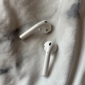 AirPods 2 - Apple AirPods 2 trådlösa hörlurar. Fungerar utmärkt och ger bra ljudkvalitet. Viss kosmetisk slitage syns på ytan, men inget som påverkar funktionen. Perfekt för musik, samtal och träning. Laddningsetui ingår ej. Lite defekter på höger utsida men inget som syns vid användning. Skriv ett rimligt pris 
