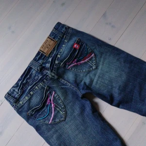 Blå bootcut jeans med broderi - Blåa jätte snygga jeans med så fina fickor. För långa på mig som är 160 cm. Nyskick! Bara dma om du undrar någonting. Midjemåttet rakt över är 36 cm. Innerbenslängden är 80 cm. Storleken är oklar på lappen men skulle säga de passar en 32/34.