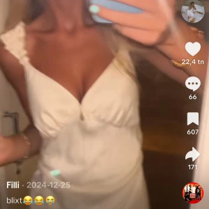 Vit kort klänning med volangband - Supersöt vit kort klänning med volangprydda axelband och v-ringning. Klänningen har en lätt utsvängd kjol och är gjord i ett glansigt material som ger en lyxig känsla. Perfekt för sommarens alla tillfällen!