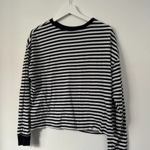 Randig långärmad tröja från H&M Divided - Svartvit långärmad tröja från H&M Divided med klassiskt horisontellt randigt mönster. Tröjan har rund halsringning med svart ribbad kant och muddar vid ärmsluten. Tillverkad i mjuk bomull, perfekt för en chill och stilren look.