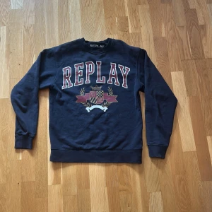 Mörkblå sweatshirt från Replay XS - Säljer en mörkblå sweatshirt från Replay i storlek XS. Tröjan har stort REPLAY-tryck och ett coolt emblem framtill. Klassisk rund hals och långa ärmar, perfekt för chill dagar. Materialet känns mjukt och skönt mot huden.