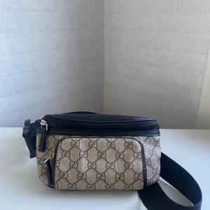 Beige magväska - Snygg beige axelväska mönster i brunt. Väskan har svarta detaljer, justerbart band och dragkedjor både fram och bak. Perfekt för att bära det viktigaste och ge din outfit en lyxig touch. Har inga synliga skador. Skriv vid intresse! 👍🏼