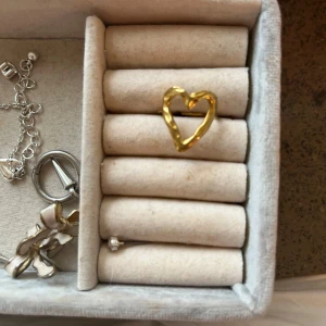 Guldig hjärtformad ring - Säljer en snygg ring i guldtonad metall med öppen hjärtformad design. Ringen har en lite ojämn, handgjord känsla och är perfekt för dig som gillar unika smycken med en romantisk touch.