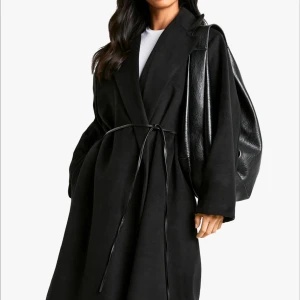 Svart kappa med bälte och bred krage - Stilren svart kappa med bred krage och knytbälte i midjan. Jackan har en rak och loose passform, långa ärmar och är tillverkad i ett mjukt ullmaterial. Perfekt för dig som gillar minimalistisk och clean look. Super skön och håller värmen ordinarie pris 1370:-