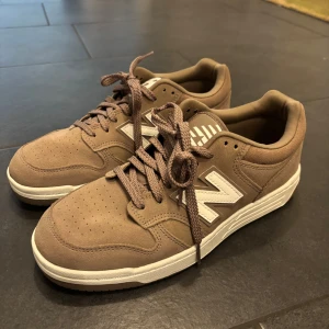 Beige New Balance 480 sneakers - Säljer ett par stilrena New Balance 480 sneakers i beige mocka med vita detaljer och klassisk N-logga på sidan. Skorna har rund tå, snörning och en vit platt sula. Perfekta för dig som gillar en clean och avslappnad look.