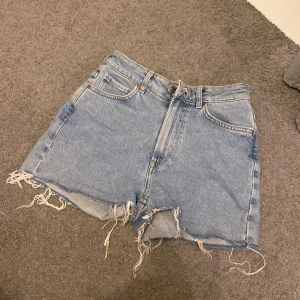 Blå jeansshorts med fransig kant XS - Snygga blå jeansshorts från Never Denim i modell mid short. De har en klassisk femficksdesign, rå och fransig kant nertill samt normal passform. Perfekta för sommaren och ger en avslappnad vibe.