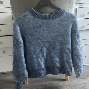 Blå stickad tröja med rund hals - Mysig blå stickad tröja med rund halsringning och ribbade muddar vid ärmslut och nederkant. Perfekt för kyliga dagar och enkel att matcha med jeans eller kjol.