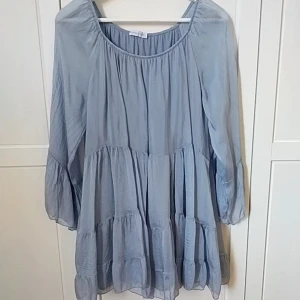 Ljusblå volangklänning Made in Italy - Superfin ljusblå klänning i bohemisk stil med volanger och lös passform. Klänningen har trekvartsärmar och är tillverkad i en mix av viskos och silke, vilket gör den både luftig och mjuk. Perfekt för sommarens varma dagar. Längd 80 cm från axeln. Oanvänd 