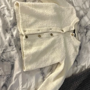 Vit kofta från Pernilla Wahlgren - Mysig vit kofta från Pernilla Wahlgren med guldiga knappar framtill. Koftan är stickad och har långärmad modell med rund halsringning. Perfekt för lager-på-lager och passar till allt.