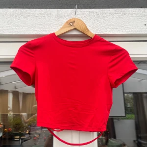 Röd croppad topp med snörning - Snygg röd croppad topp med korta ärmar och cool snörningsdetalj baktill. Toppen har rund halsringning och är tillverkad i ett mjukt bomullsmaterial. Perfekt för dig som vill sticka ut med en färgstark och trendig look.