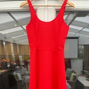 Röd kortklänning - Snygg röd klänning med rundad urringning. Modellen är figurnära upptill och har en lätt utställd kjol som ger en klassisk siluett. Perfekt för dig som vill sticka ut med en färgstark look.