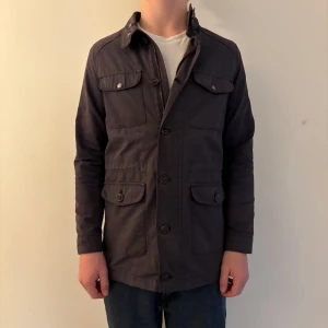 Mörkblå trenchcoat från Massimo Dutti - Säljer en mörkblå jacka från Massimo Dutti med fyra fickor framtill och snygga knappar. Jackan har klassisk krage och är helfodrad. Tillverkad i bomull och polyester, perfekt för dig som gillar stilren och tidlös design. Modellen är 175 cm lång och väger 63kg. (Jackan sitter tajt!). Jackan är i storlek 158-166 men passar mer som en XS! (Plagget skickas inom 24h efter köp!) hör av dig vid frågor!