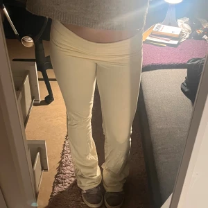 lågmidjade bootcut yoga pants   - Säljer ett par riktigt snygga lågmidjade yoga tihgts i vit/cream färg. De har bootcut-modell med utsvängda ben och sitter tajt upptill. Mjukt och stretchigt material som är skönt att ha på sig. Perfekta för dig som gillar trendiga och bekväma byxor.
