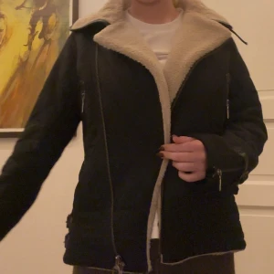 Jacka från Barbour - Jacka från Barbour med mysigt beige foder i teddy, dragkedjor på fickor och ärmslut samt snygga spänndetaljer i sidorna. Jackan har en klassisk krage och lång ärm, perfekt för kyliga dagar. Original pris 4000