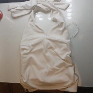 Vit tröja med knyt - Supersöt vit tröja med omlott och breda knytband i halsen. Tröjan har v-ringning och är ärmlös, perfekt för varma dagar. Materialet känns mjukt och följsamt mot huden. Enkel men ändå stilren design som sticker ut med sin knytning. Har en liten fläck inne🤍