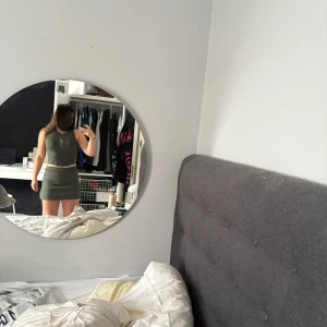 Olivgrön tight kortklänning - Säljer en olivgrön tight kortset med ärmlös design och rund halsringning. Settet har en enkel, stilren look med en liten vit detalj framtill. Perfekt för dig som gillar minimalistisk och sportig stil.