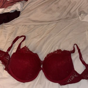 Vinröd spetskorsett med vaddering - Säljer en vinröd korsett med vadderade kupor och fina spetsdetaljer längs kanterna. Axelbanden är justerbara och sidorna har transparent spets för en extra snygg look. Perfekt för dig som vill ha något både bekvämt och snyggt.