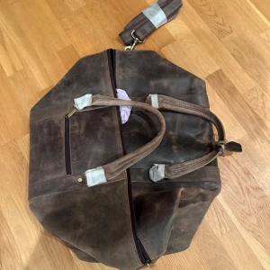 Brun weekendbag i skinn från Velorbis - Snygg och rymlig weekendbag från Velorbis i mörkbrunt skinn. Väskan har robusta handtag, avtagbar axelrem och dragkedja upptill. Perfekt för resor med sin klassiska look och praktiska innerfack. Kommer med original dustbag. Nypris ca 5500. Aldrig använd!