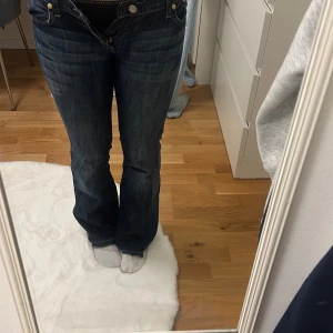Mörkblå bootcut jeans med broderi - Säljer ett par mörkblå bootcut jeans från Rock & Republic med snyggt guldigt broderi på bakfickan. Jeansen har låg midja, klassisk femficksdesig. Dom är omsydda där nere för mer bootcut. Pris kan diskuteras🥰