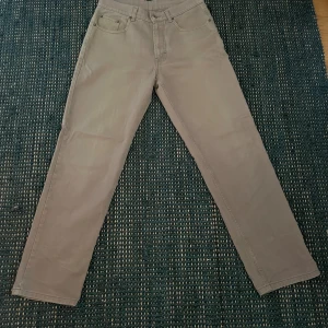 Gråa jeans från MC.Gordon - 38 cm i midjan mätt rakt över och 106 i ytterbenslängd. Gråa jeans från MC.Gordon i klassisk rak modell. Byxorna är tillverkade i 100% bomull och har fem fickor samt bälteshällor. Snyggt minimalistisk look som passar till det mesta. Classic fit med raka ben och normal passform. 