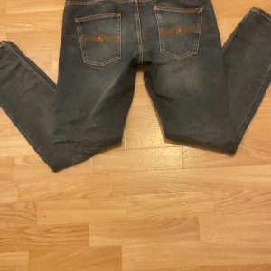 Nudie Jeans blå jeansbyxor W33 L32 - Säljer ett par klassiska blå jeans från Nudie Jeans med snygga orange sömmar och ikonisk broderad bakficka. Jeansen har normal passform och är tillverkade i slitstarkt bomullsjeans. Perfekta för dig som gillar stilrena och tidlösa jeans. Nypris 1600. Skicket är oerhört bra, använda väldigt fåtal gånger. Skick: 9,5/10. Priset kan absolut diskuteras!