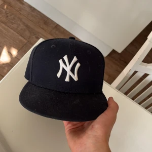Svart New Era Yankees keps - Klassisk svart New Era keps med New York Yankees-logga broderad i vitt framtill. Kepsen har rak skärm och broderade ventilationshål. Materialet är bomull och kepsen har en stilren och sportig look som passar perfekt till streetwear
