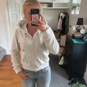 Vit hoodie från Juicy Couture - Säljer en klassisk vit hoodie från Juicy Couture i storlek L. Tröjan har dragkedja framtill, snörning i huvan och ribbade muddar. Mjuk och skön, perfekt för chill dagar. 