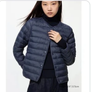 Mörkblå uniqlo jacka - Säljer en stilren mörkblå dunjacka med rund halsringning och tryckknappar framtill. Jackan är quiltad och har en lätt, smidig passform som funkar perfekt till lager-på-lager. Klassisk look utan huva och med långa ärmar.