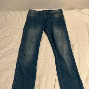 Replay Anbass - Säljer ett par klassiska blå jeans från Replay med snyggt slitna detaljer och raka ben. Jeansen har fem fickor, läderpatch bak och diskret Replay-logga. Perfekt passform och tillverkade i mjukt denimtyg för en skön känsla.